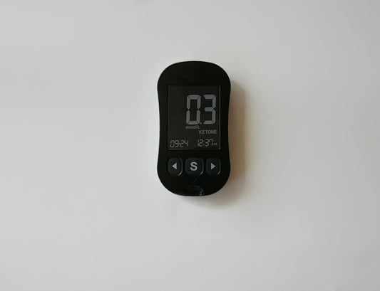 A close-up of a digital ketone meter displaying readings on a white surface.