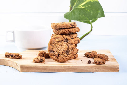 Close-up of chocolate chip cookies on a wooden board with a cup in the background.