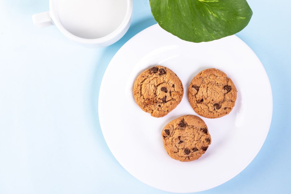 Delicious chocolate chip cookies on a white plate with a cup of milk and a green leaf in view.