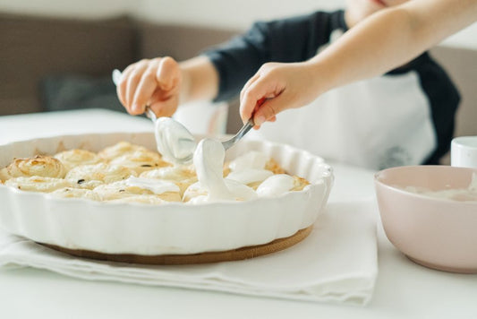 Kids having fun with homemade cinnamon rolls and cream in a cozy indoor setting.
