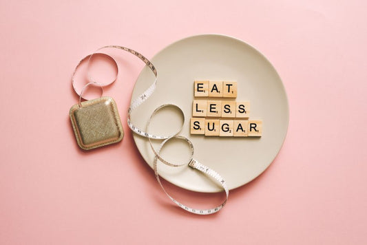 Flat lay of Scrabble tiles saying 'Eat Less Sugar' on a plate with a tape measure on a pink background.