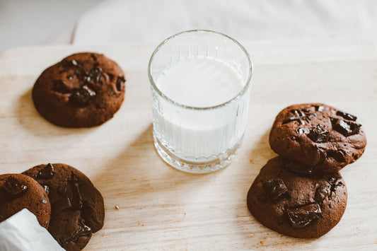 Delicious chocolate chip cookies and a glass of milk on a wooden board, perfect for a sweet treat.