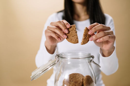 Close-up of a woman breaking a cookie over a glass jar filled with cookies.