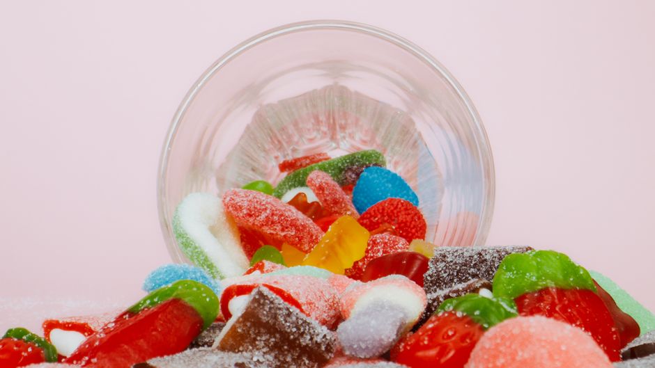 Vibrant sweet gummies spilling from a bowl on a pastel background.