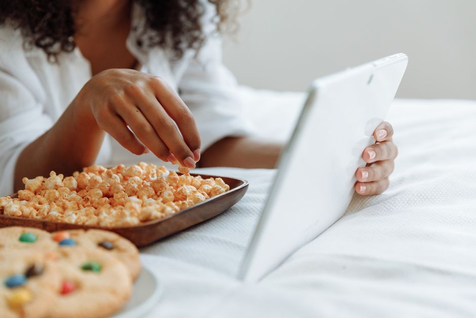 A woman enjoys snacks while using a tablet in a cozy indoor setting, highlighting leisure and relaxation.