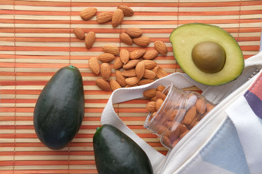 Top view of fresh avocados and almonds in a glass jar on a bamboo mat, perfect for healthy snacking.