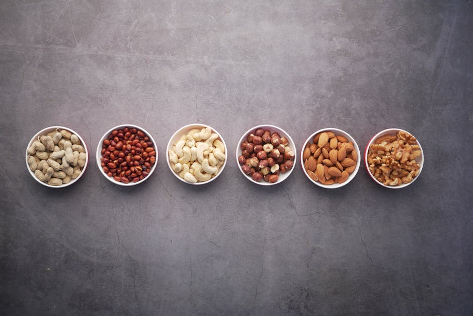 Flat lay of assorted nuts in bowls on a textured gray surface, highlighting healthy food options.