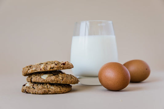 A cozy breakfast setting with cookies, fresh eggs, and a glass of milk on a neutral background.